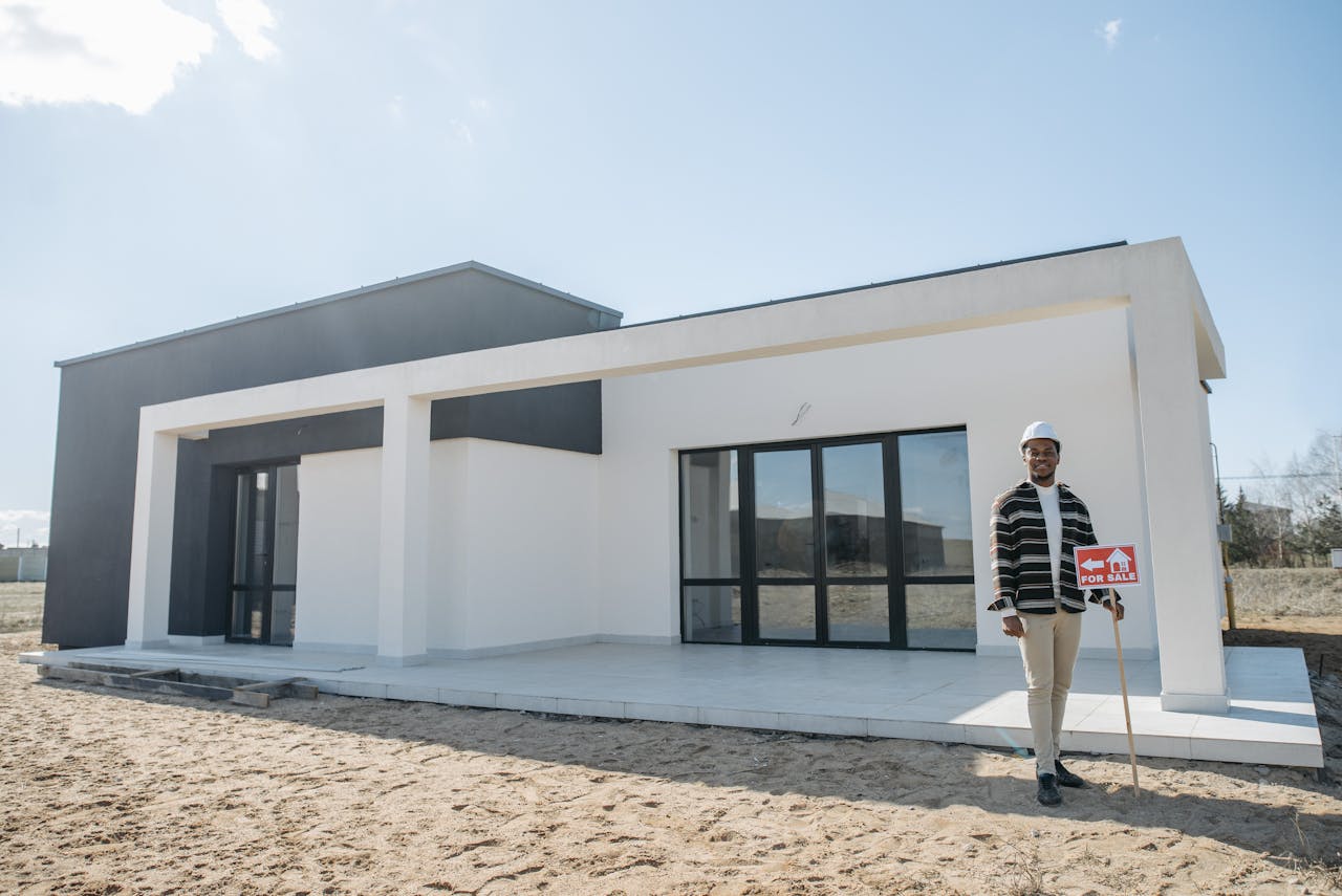 A realtor stands with a for sale sign in front of a modern house.